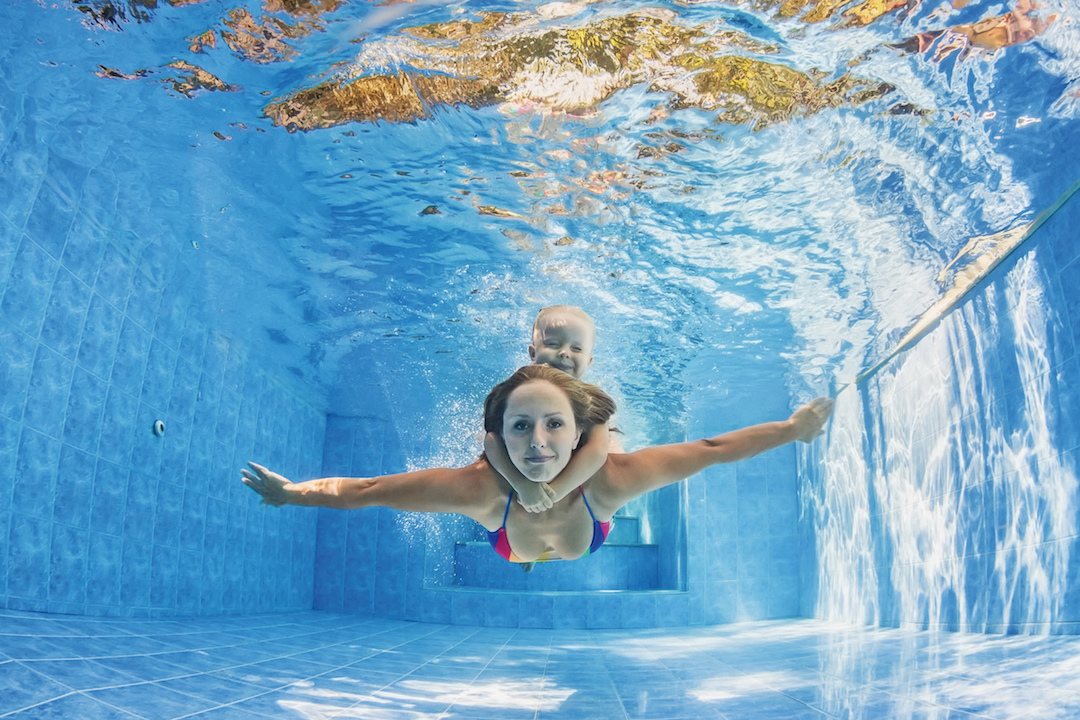 Mother with child swimming and diving underwater in pool